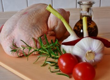 Hähnchen auf einem Holzbrett neben Zwiebeln, Tomaten und Knoblauch