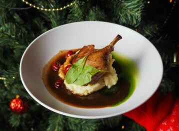 Entenkeule auf Kartoffelbrei vor Weihnachtsbaum.